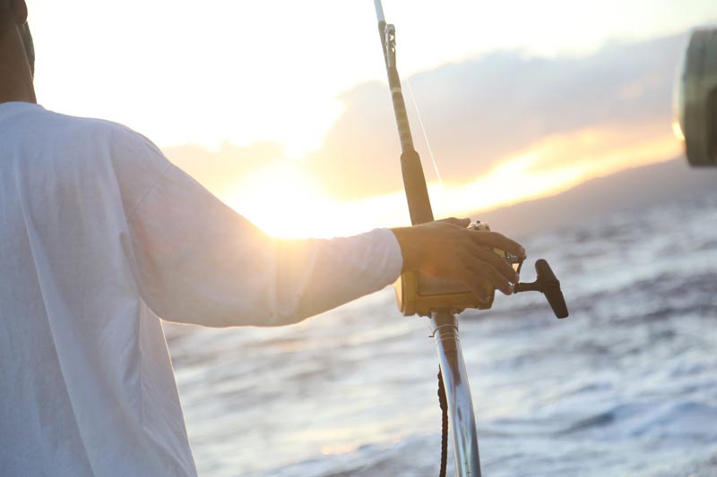 A fisher on a charter boat with rod and reel looking out over the ocean