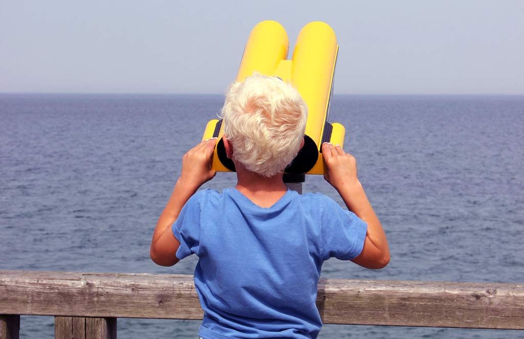 Kid looking through binoculars at beach doing "reconnaissance"